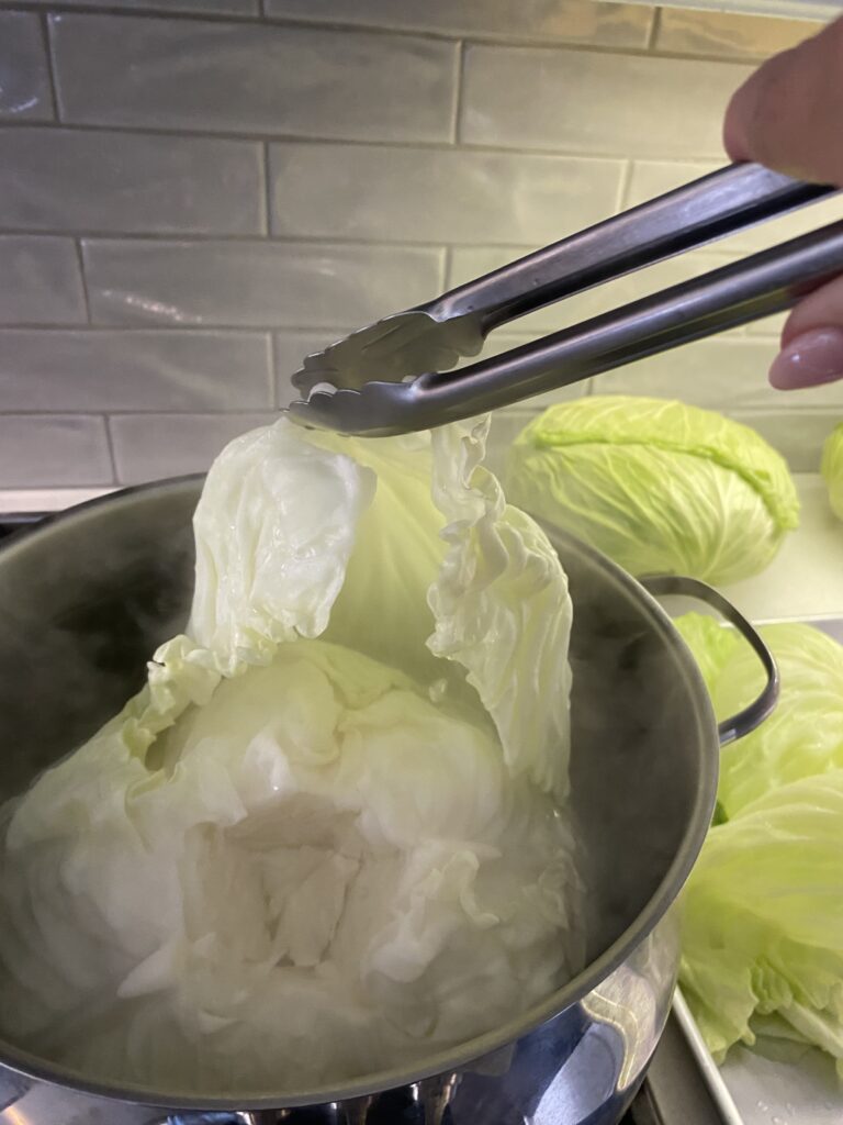 Lifting a softened cabbage leaf from hot water with tongs for homemade cabbage rolls