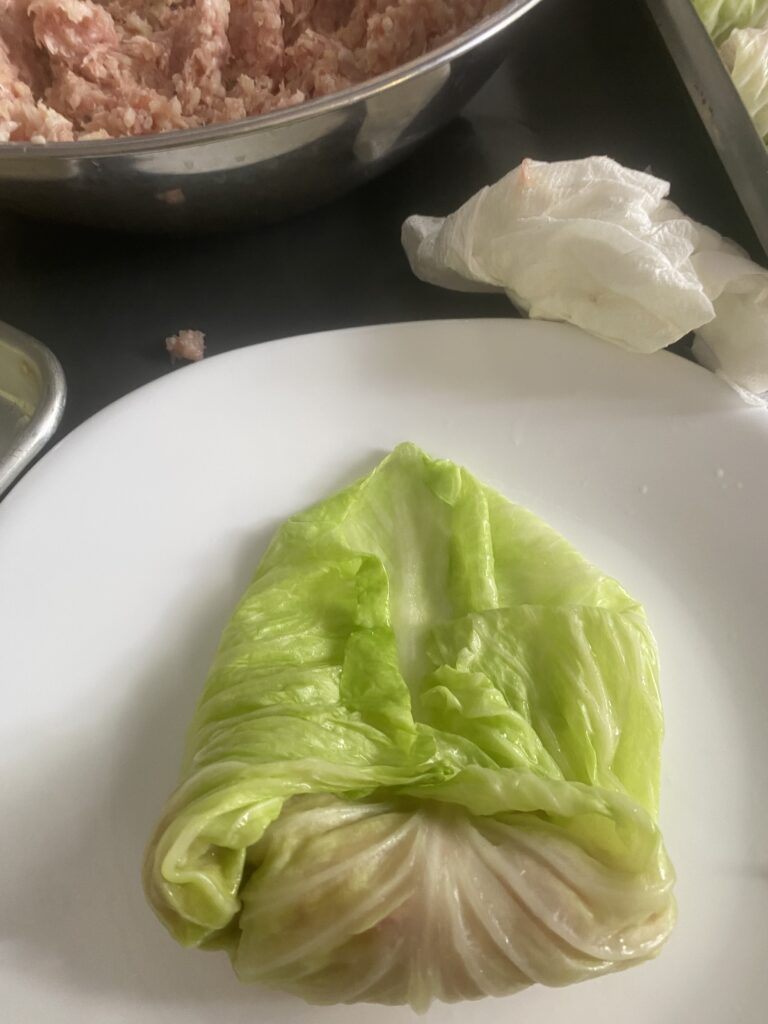 Folding the sides of a cabbage leaf over the pork and rice filling
