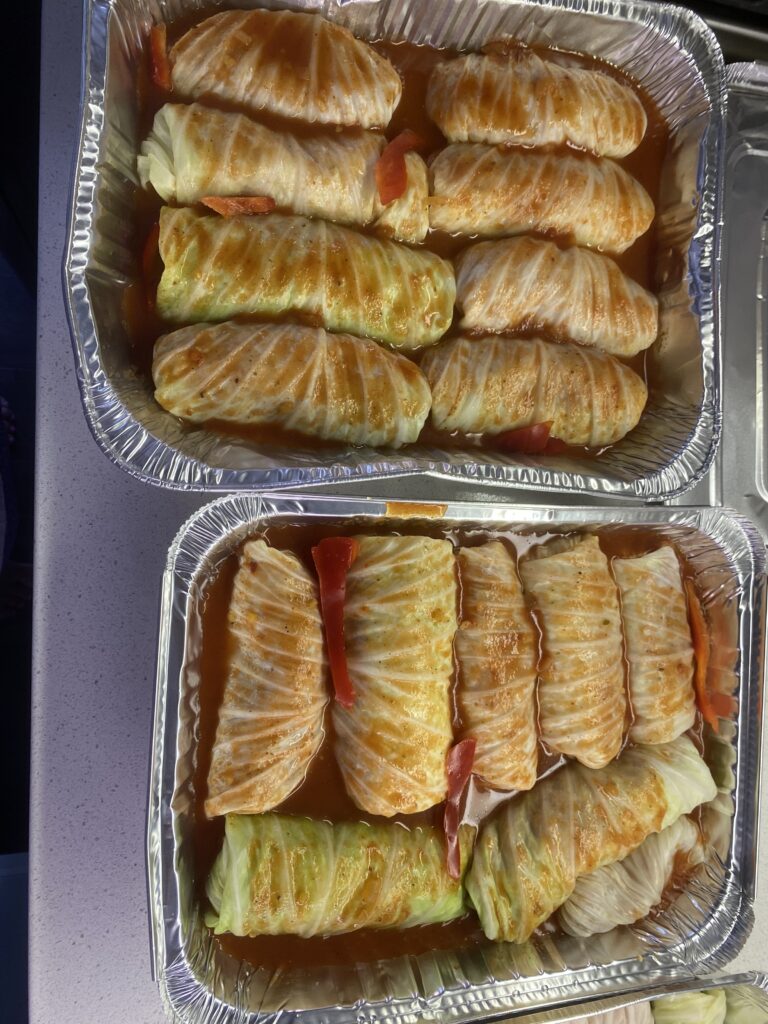 Homemade cabbage rolls arranged in a baking pan with tomato sauce and red pepper slices before baking